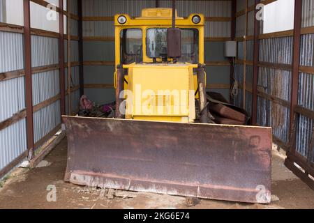 Großer Radtraktor mit Planierschild zum Freiräumen von Straßen von Schnee. Gelber Radlader in der Garage. Stockfoto