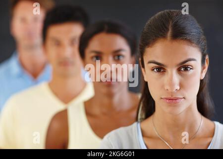 Konzentrieren Sie sich darauf, sich herauszustellen. Porträt einer attraktiven jungen Frau, die unscharf mit ihren Gleichaltrigen in Einklang steht. Stockfoto