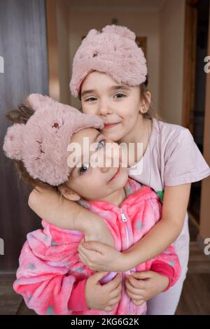 Zwei weiße Mädchen umarmen und lächeln im Pyjama im Zimmer. Auf den Augen sind lustige Verbände zum Schlafen. Hochwertiges Foto Stockfoto