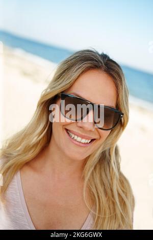 Jede Minute im Paradies lieben. Kopf- und Schulterporträt einer attraktiven jungen Frau, die an einem sonnigen Strand steht. Stockfoto