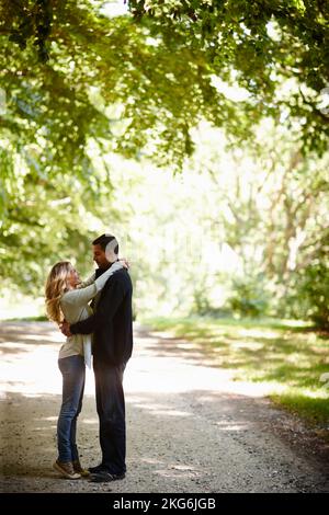 Nehmen Sie einen ruhigen romantischen Moment zusammen. Die ganze Aufnahme eines jungen Paares, das sich umarmt, während er einen Tag im Park genießt. Stockfoto