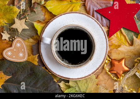 Leere Porzellanschale mit einem herzförmigen Keks auf einer Untertasse, umgeben von bunten Herbstblättern, perfekt für eine gemütliche Herbstkulisse. Stockfoto