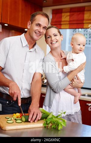 Was ist Papa Kochen. Ein Porträt eines glücklichen Paares, das sein Baby hält, während es in der Küche steht. Stockfoto