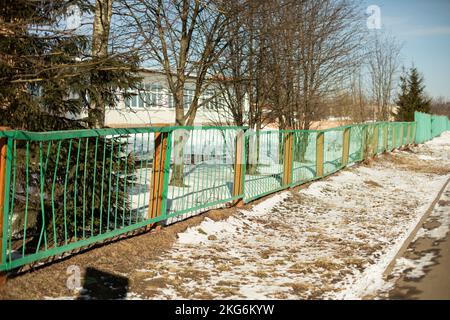 Zäune um die Schule im Winter. Grüner Zaun in der Stadt. Privates Territorium. Straßendetails. Stockfoto