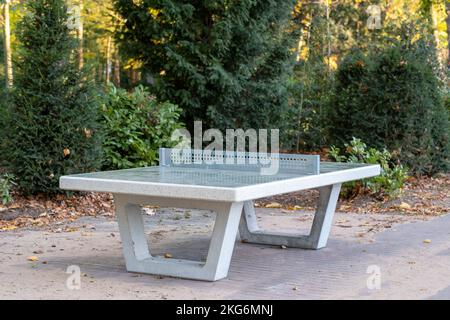 Tischtennisplatte aus Beton im Freien in einem Park, umgeben von üppigen grünen Bäumen und Sträuchern, ideal für Freizeitaktivitäten und Sportbegeisterte Stockfoto