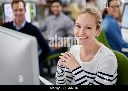 Jeder liebt sie. Hochwinkelporträt einer lächelnden Geschäftsfrau mit ihren Mitarbeitern im Hintergrund. Stockfoto