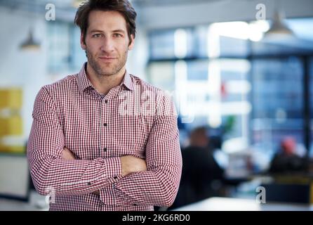 Ich weiß, dass ich die richtigen Schritte mache. Ein gutaussehender Mann, der ernsthaft auf die Kamera blickt, hinter dem sich ein offener Bürobereich befindet. Stockfoto