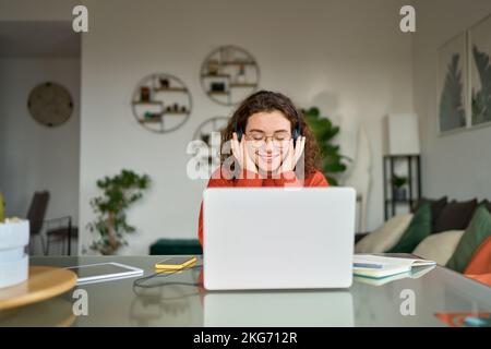 Junge lächelnde Frau mit Kopfhörern, die Podcast-Musik hört und zu Hause lernt. Stockfoto