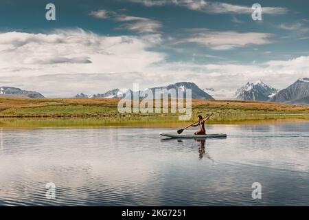 Ein wunderschönes, sportliches Mädchen in der Bikinizone geht auf einem Stehpaddelbrett am Mountain Lake spazieren Stockfoto