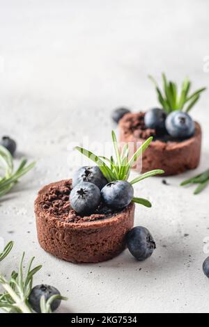 Zwei Schokoladen-Brownies mit Blaubeeren und Rosmarin auf weißem Strukturhintergrund. Weihnachten, Neujahr Rezept Konzept. Platz für Text. Verti Stockfoto