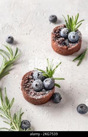 Zwei Schokoladen-Brownies mit Heidelbeeren und Zuckerpulver auf weißem strukturiertem Hintergrund. Weihnachten, Neujahr Rezept Konzept. Vertikale Ausrichtung Stockfoto