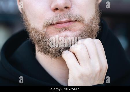 In Nahaufnahme berührt ein junger Mann seinen Bart mit der Hand. Stockfoto