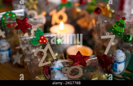 ILLUSTRATION - 21. November 2022, Berlin: Ein selbstgemachter Adventskalender mit kleinen Tüten mit Zahlen von 1 bis 24, gefüllt mit Weihnachtsgebäck und Schokolade, steht neben zwei Kerzen auf einem Tisch. Foto: Monika Skolimowska/dpa Stockfoto