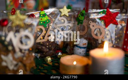 ILLUSTRATION - 21. November 2022, Berlin: Ein selbstgemachter Adventskalender mit kleinen Tüten mit Zahlen von 1 bis 24, gefüllt mit Weihnachtsgebäck und Schokolade, steht neben zwei Kerzen auf einem Tisch. Foto: Monika Skolimowska/dpa Stockfoto