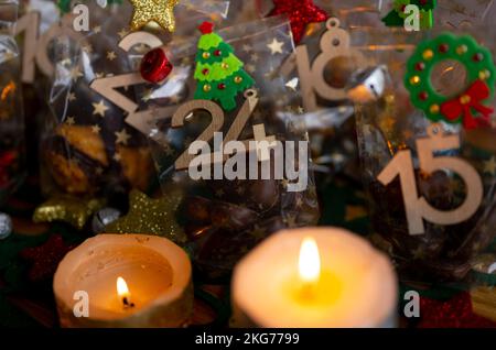 ILLUSTRATION - 21. November 2022, Berlin: Ein selbstgemachter Adventskalender mit kleinen Tüten mit Zahlen von 1 bis 24, gefüllt mit Weihnachtsgebäck und Schokolade, steht neben zwei Kerzen auf einem Tisch. Foto: Monika Skolimowska/dpa Stockfoto