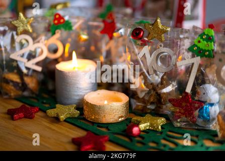 ILLUSTRATION - 21. November 2022, Berlin: Ein selbstgemachter Adventskalender mit kleinen Tüten mit Zahlen von 1 bis 24, gefüllt mit Weihnachtsgebäck und Schokolade, steht neben zwei Kerzen auf einem Tisch. Foto: Monika Skolimowska/dpa Stockfoto