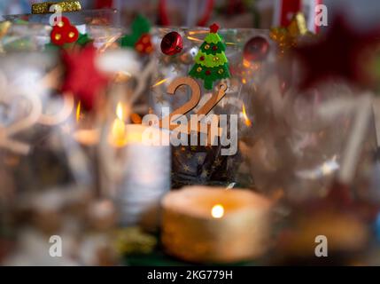 ILLUSTRATION - 21. November 2022, Berlin: Ein selbstgemachter Adventskalender mit kleinen Tüten mit Zahlen von 1 bis 24, gefüllt mit Weihnachtsgebäck und Schokolade, steht neben zwei Kerzen auf einem Tisch. Foto: Monika Skolimowska/dpa Stockfoto