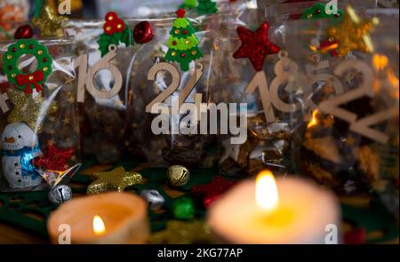 ILLUSTRATION - 21. November 2022, Berlin: Ein selbstgemachter Adventskalender mit kleinen Tüten mit Zahlen von 1 bis 24, gefüllt mit Weihnachtsgebäck und Schokolade, steht neben zwei Kerzen auf einem Tisch. Foto: Monika Skolimowska/dpa Stockfoto