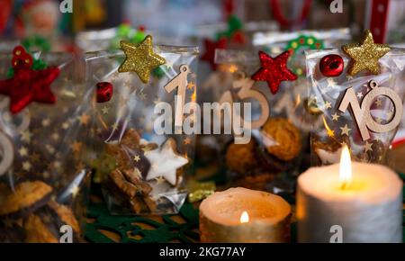 ILLUSTRATION - 21. November 2022, Berlin: Ein selbstgemachter Adventskalender mit kleinen Tüten mit Zahlen von 1 bis 24, gefüllt mit Weihnachtsgebäck und Schokolade, steht neben zwei Kerzen auf einem Tisch. Foto: Monika Skolimowska/dpa Stockfoto