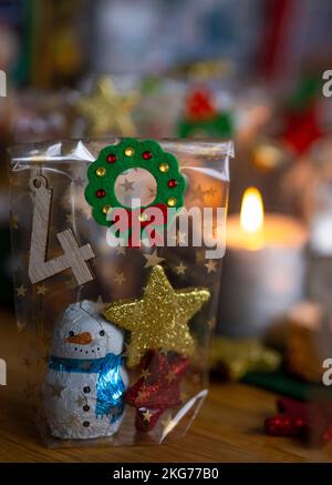 ILLUSTRATION - 21. November 2022, Berlin: Ein selbstgemachter Adventskalender mit einer kleinen Tüte mit der Nummer 4, gefüllt mit Weihnachtsgebäck und Schokolade, steht neben einer Kerze auf einem Tisch. Foto: Monika Skolimowska/dpa Stockfoto