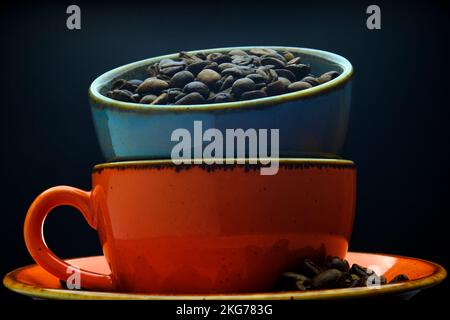 Übereinander gestapelte Porzellanbecher, gefüllt mit frischen Kaffeebohnen, in einer Makroaufnahme vor schwarzem Hintergrund Stockfoto