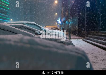 Nahaufnahme von verschneiten Hauben von Autos, die an einem verschneiten Abend auf dem Parkplatz in Reihe stehen Stockfoto
