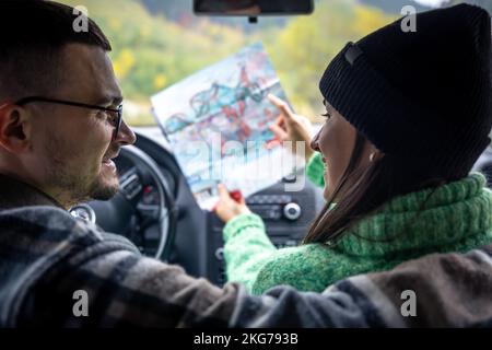 Ein Mann und eine Frau, die Papierkarte halten und betrachten, sitzen im Auto. Stockfoto