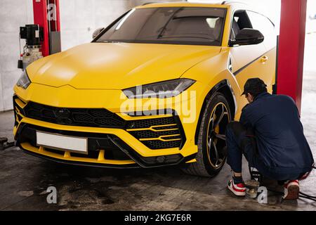 Der Mechaniker überprüft den Reifendruck im gelben Sportwagen-suv. Stockfoto