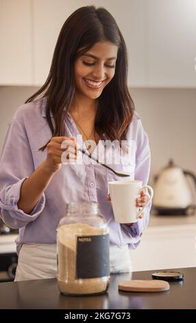 Frau, Lächeln und morgens Kaffee in der Küche für Routine, Start oder tägliche Vorbereitung zu Hause. Frau lächelt und Zucker in den Becher geben Stockfoto