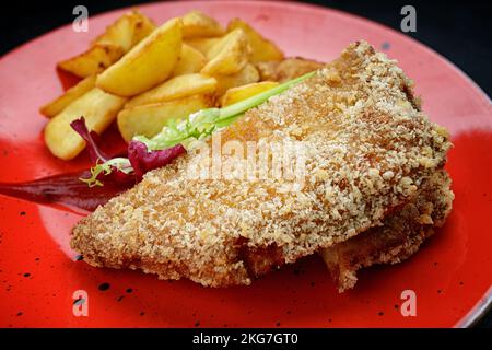 Schweineschnitzel mit Kartoffeln, Soße und Kräutern auf einem roten Teller Stockfoto