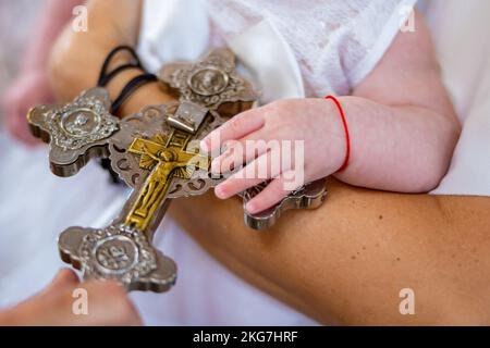 Das christliche Baby überreicht das goldene silberne Kreuz eines Priesters in einer Kirche. Die Taufe der Kindertaufe. Hochwertiges Foto Stockfoto