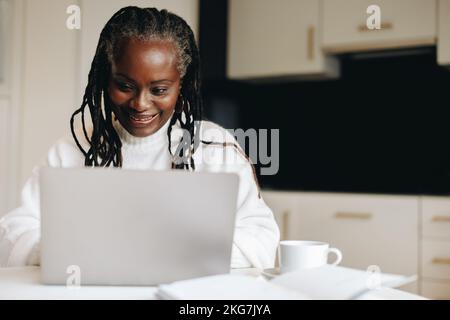 Reife Geschäftsfrau, die zu Hause mit einem Notebook tippt und dabei glücklich lächelt. Geschäftsfrau, die von zu Hause aus eine geschäftliche E-Mail versendet. Stockfoto