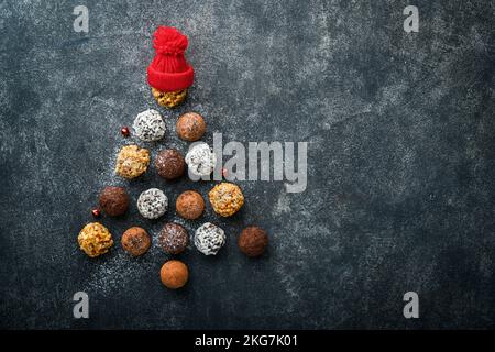 Weihnachtsbaum aus Schokoladentrüffeln, Haselnüssen, Anissternen, Dekorationen, Löffeln und pulverförmiges Zuckerschnee auf dunklem Grund. Weihnachtsfeiertage c Stockfoto