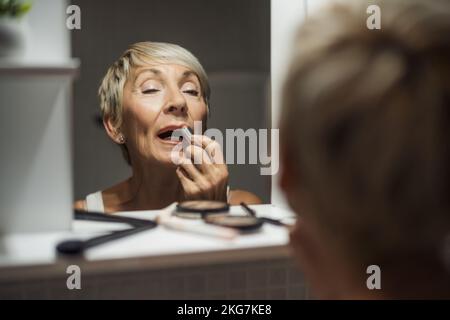 Eine Erwachsene Frau trägt Lippenstift im Badezimmer auf. Stockfoto