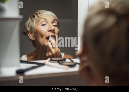 Eine Erwachsene Frau trägt Lippenstift im Badezimmer auf. Stockfoto