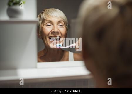 Reife Frau putzt sich im Badezimmer die Zähne. Stockfoto