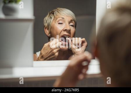 Reife Frau benutzt Zahnseide, um ihre Zähne zu reinigen. Stockfoto