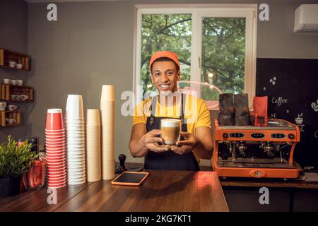 Fröhlicher junger Barista, der einem Gast Kaffee serviert Stockfoto