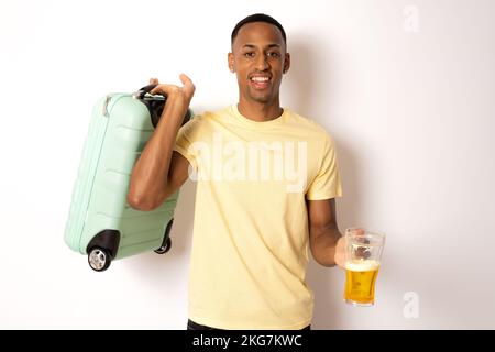 Junger gutaussehender Mann auf isoliertem weißen Hintergrund im Urlaub mit Reisekoffer und Bier trinken. Stockfoto