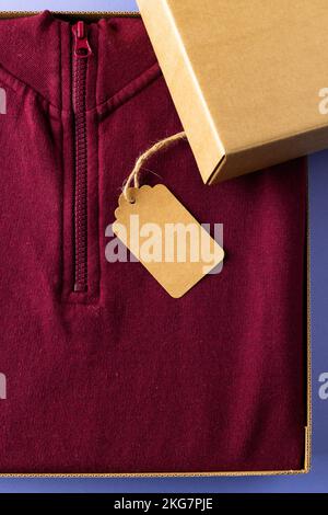 Nahaufnahme des roten Sweatshirts mit Anhänger in der Verpackung und Kopierbereich auf blauem Hintergrund Stockfoto