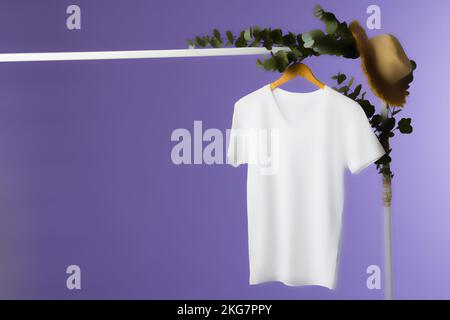 Das T-Shirt hängt am Kleiderbügel und kopiert auf lila Hintergrund Stockfoto