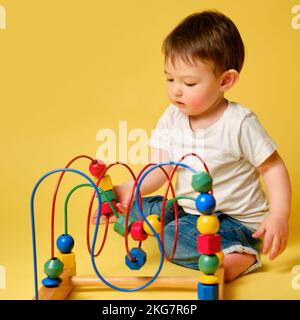 Kleinkind Baby spielt Logik pädagogische Spiele auf einem Studio gelben Hintergrund. Glückliches Kind spielen mit Lernspielzeug, Lernlogik. Kind im Alter von einem, ja Stockfoto