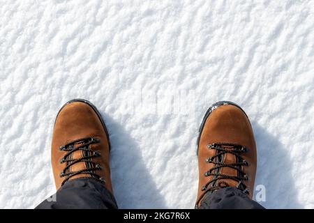 Nahaufnahme von oben auf männliche Fußfüße in braunen Lederstiefeln isoliert auf weißem eiskaltem Schneehintergrund. Details wasserdichte Schuhe. Im Winter Stockfoto