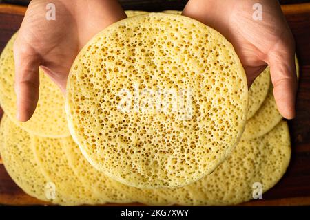 Eine Hand nimmt einen marokkanischen Pfannkuchen, Baghrir typisch marokkanisches Frühstücks-Dessert Stockfoto