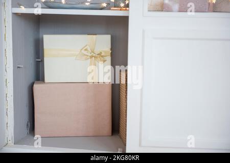 In einem weißen Anrichte aus Holz sind pinke Weihnachtsboxen mit einem goldenen Band gebunden. Eine helle Girlande sorgt für eine festliche Atmosphäre im Haus. Christma Stockfoto