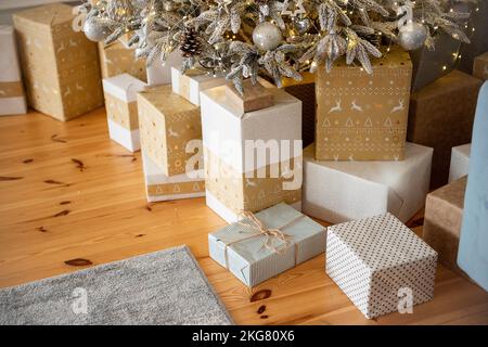 Holzboden, Laminat, Schachteln mit Geschenken in weißem Craft-Gold-Papier unter dem Weihnachtsbaum. Warten auf Weihnachten, Weihnachtsmann. Künstlicher Luxus Chr. Stockfoto