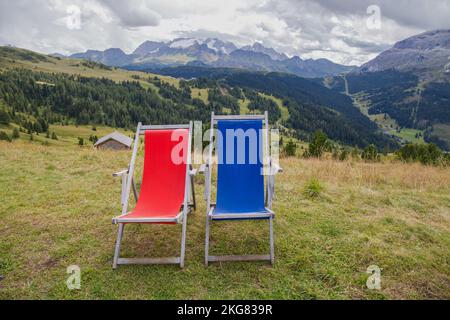 Ein paar rote und blaue Liegestühle in der dolomitischen Landschaft mit Marmolada im Hintergrund, Südtirol, Bozen Provinz, Italien Stockfoto