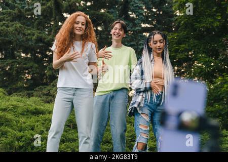 Eine Gruppe von Freunden in einem Stadtpark, die nach der Universität ein Online-Video auf dem Telefon aufgezeichnet haben. Sommerliche Mode. Halten Sie den Moment fest Stockfoto