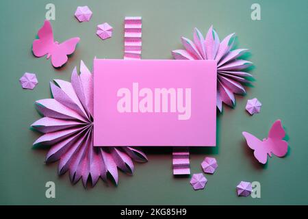 Papierfächer, Schmetterlinge, Blumen. Dekorativer Rahmen für leere Grußkarte. Flaches Lay mit Frühlings-Ornamenten, Dekorationen auf grauem Hintergrund. Geburtstag Stockfoto