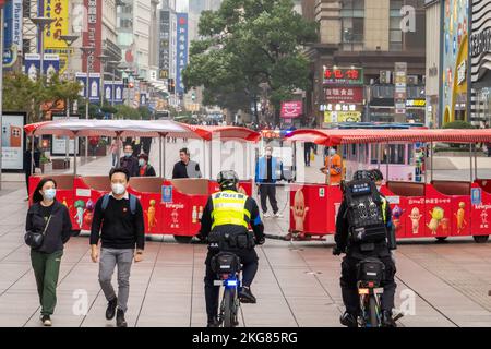 SHANGHAI, CHINA - 22. NOVEMBER 2022 - zwei voll ausgestattete Polizeibeamte fahren Fahrräder, um die Fußgängerzone Nanjing Road in Shanghai, China, zu patrouillieren Stockfoto